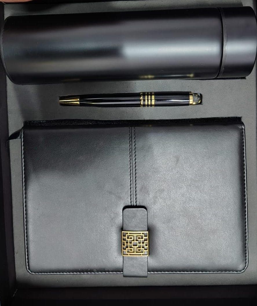 Matte black insulated flask, black and gold pen, and leather folio with antique-brass clasp seated in a black gift tray