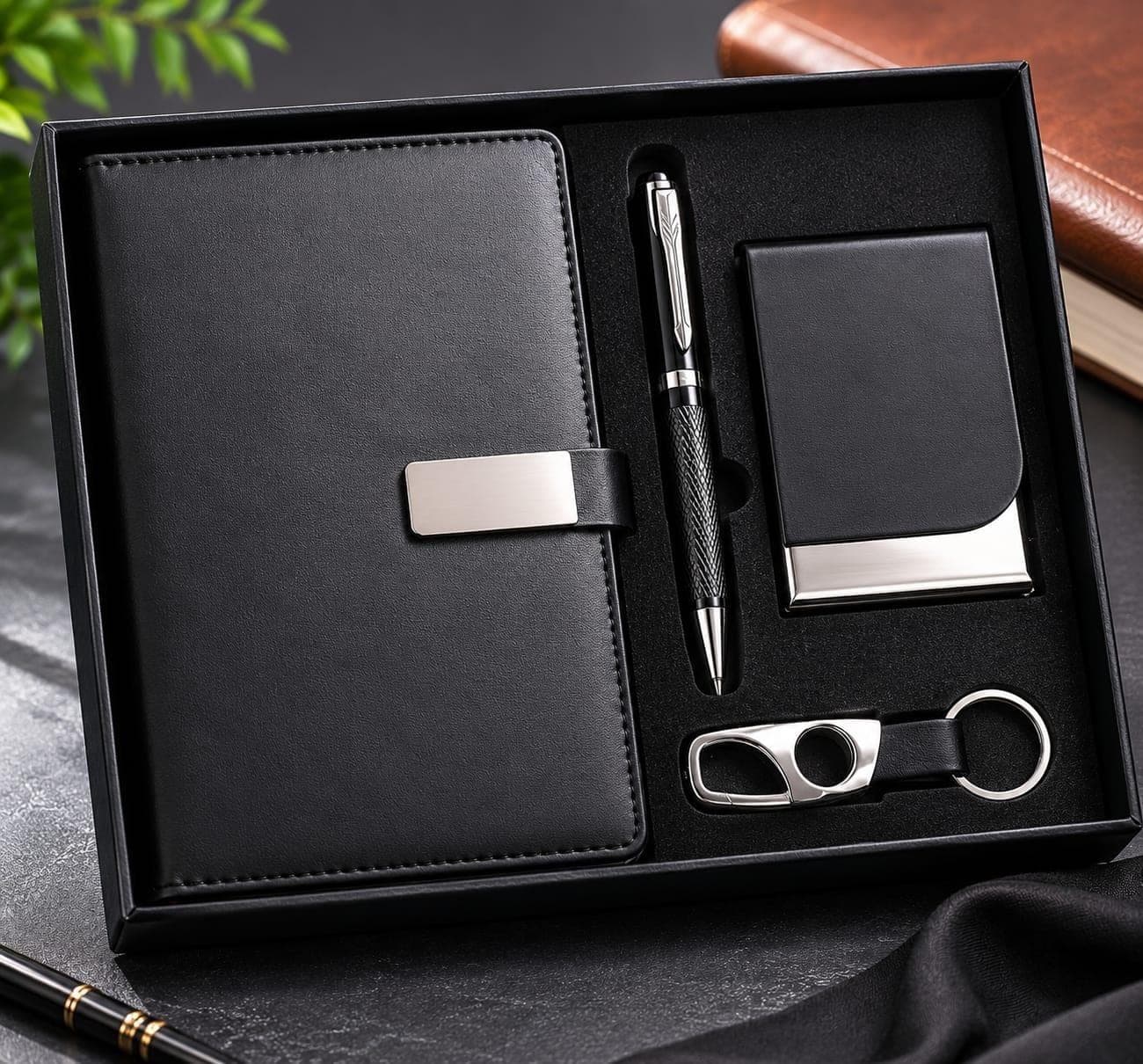 Black notebook with brushed-steel clasp, knurled pen, steel-trimmed card case and steel keychain in a black presentation box